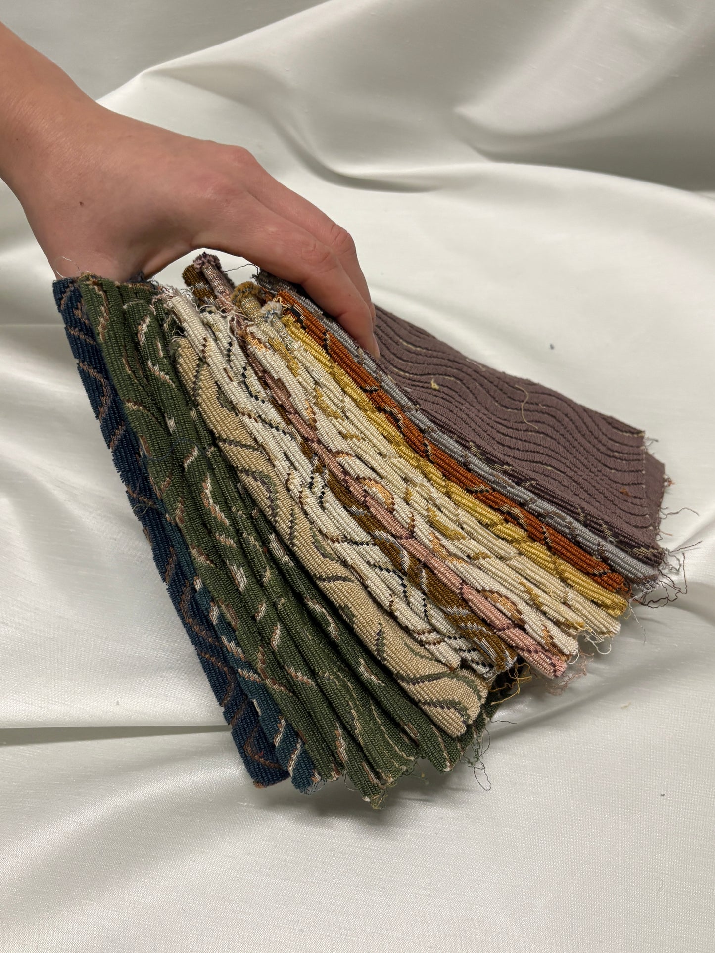 Hand holding a stack of textured fabric samples against a white background