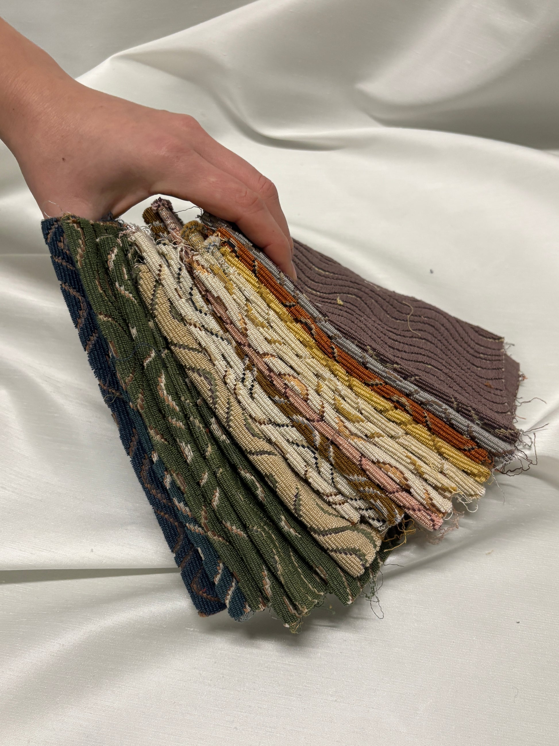 Hand holding a stack of textured fabric samples against a white background