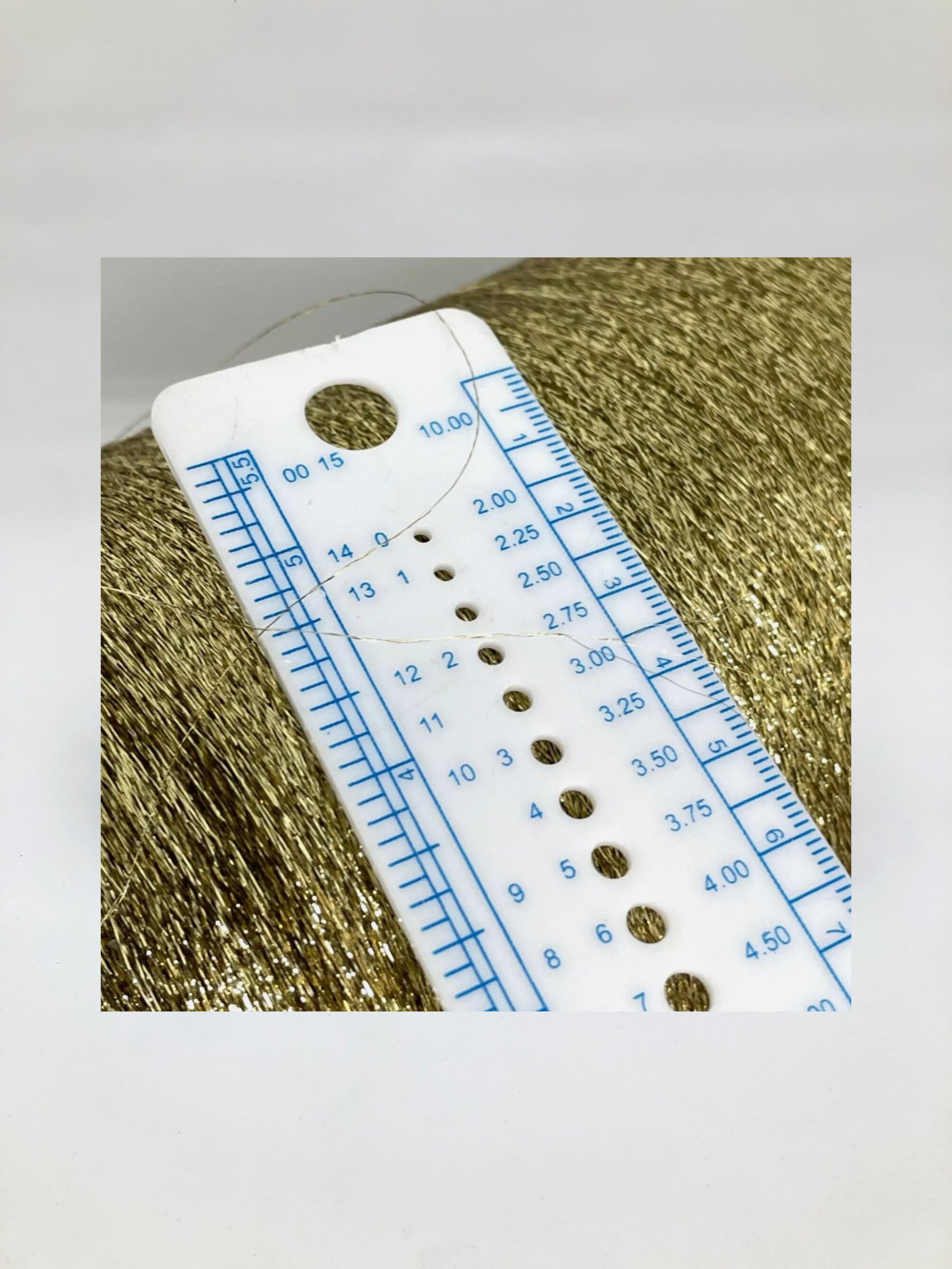 Close up of a metallic gold yarn and a ruler showing how thin yarn is.