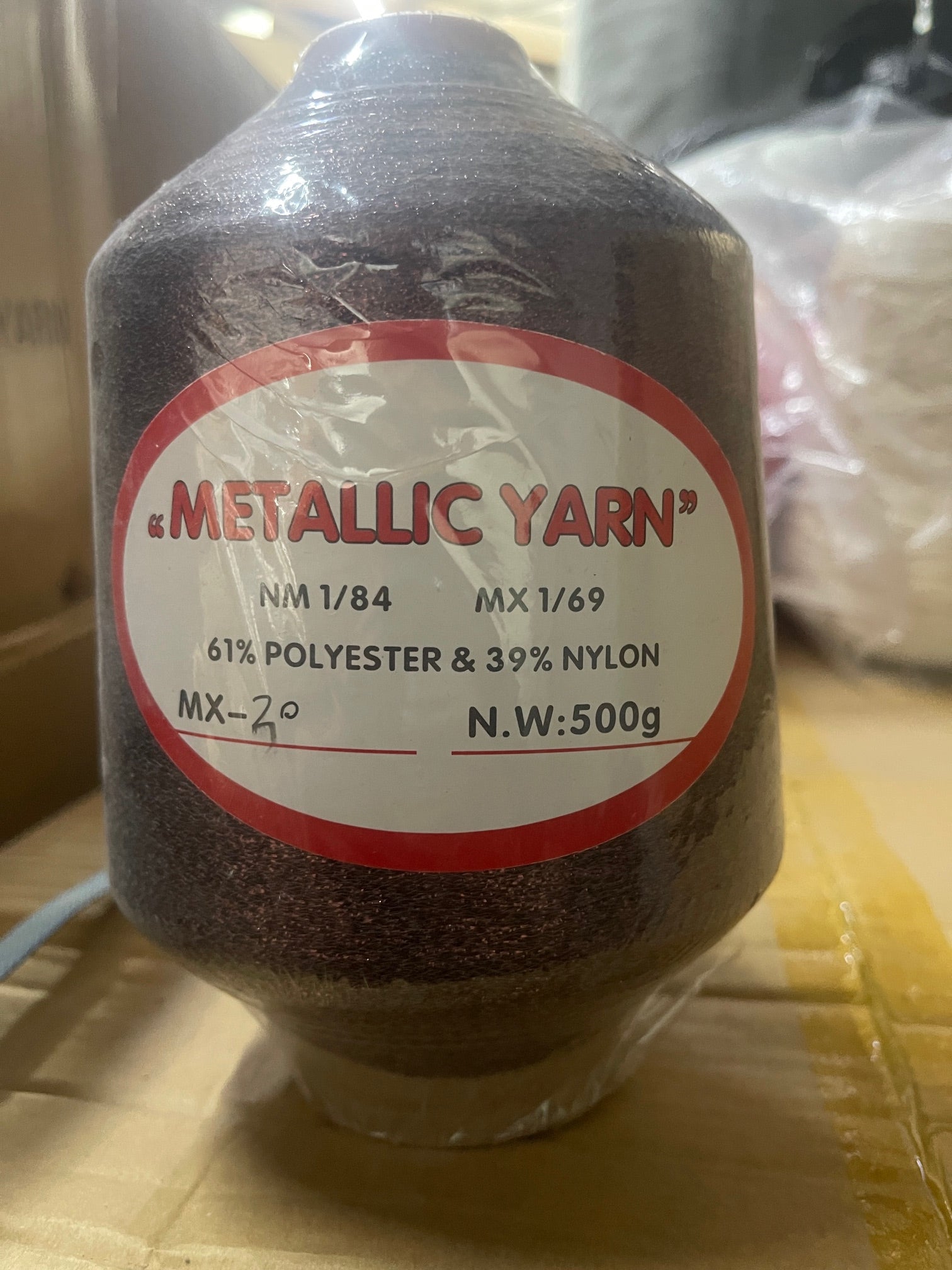 A close up of a yarn cone for knitting machine in colour metallic brown with a sticker that contains the content of the fibre. 