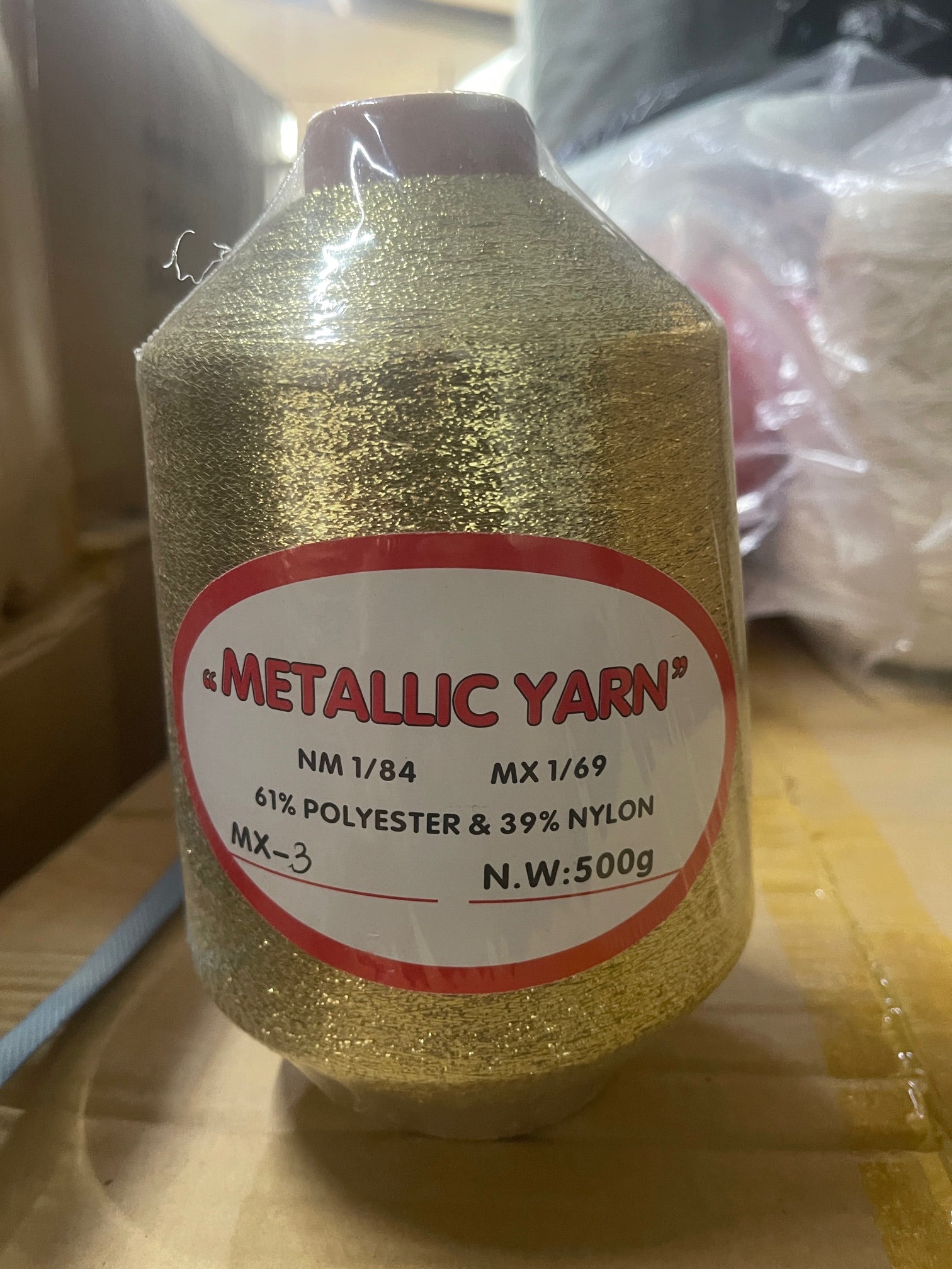 A close up of a yarn cone for knitting machine in colour gold with a sticker that contains the content of the fibre. 