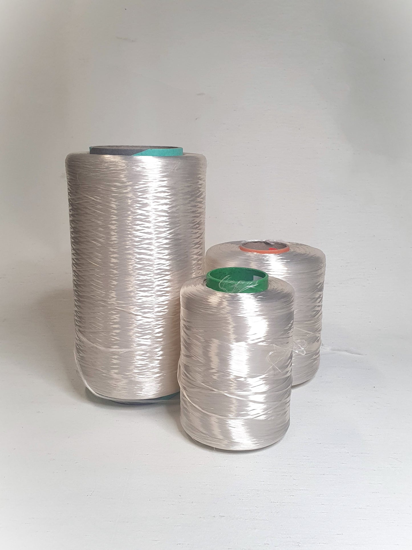 Three cones of rayon multifilament yarn with different thicknesses placed on a light background.