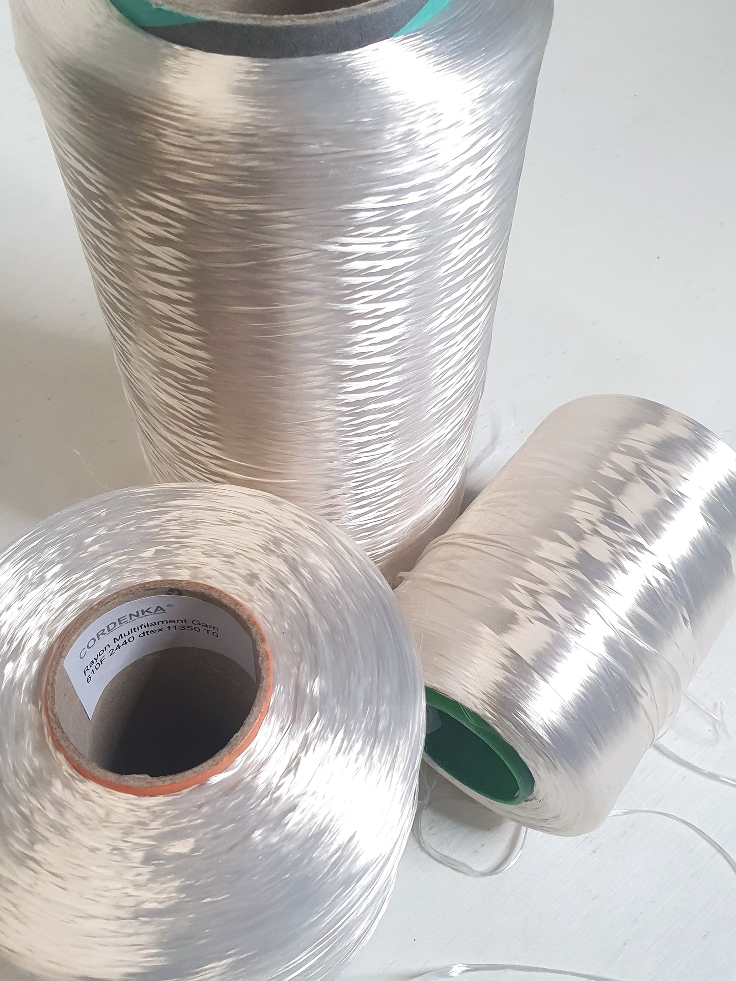 Close up of three cones of rayon multifilament yarn with different thicknesses placed on a light background.