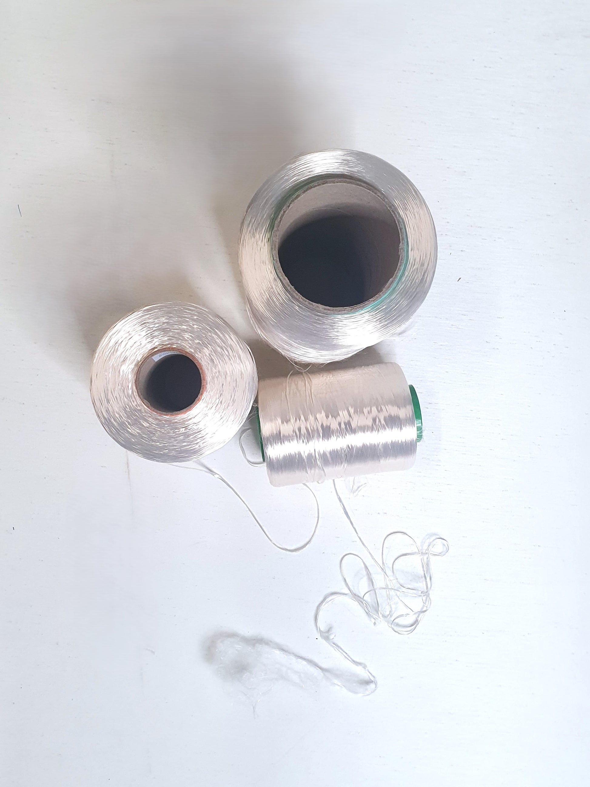 Close up of three cones of rayon multifilament yarn with different thicknesses placed on a light background from their top showing how thick the cones are. 