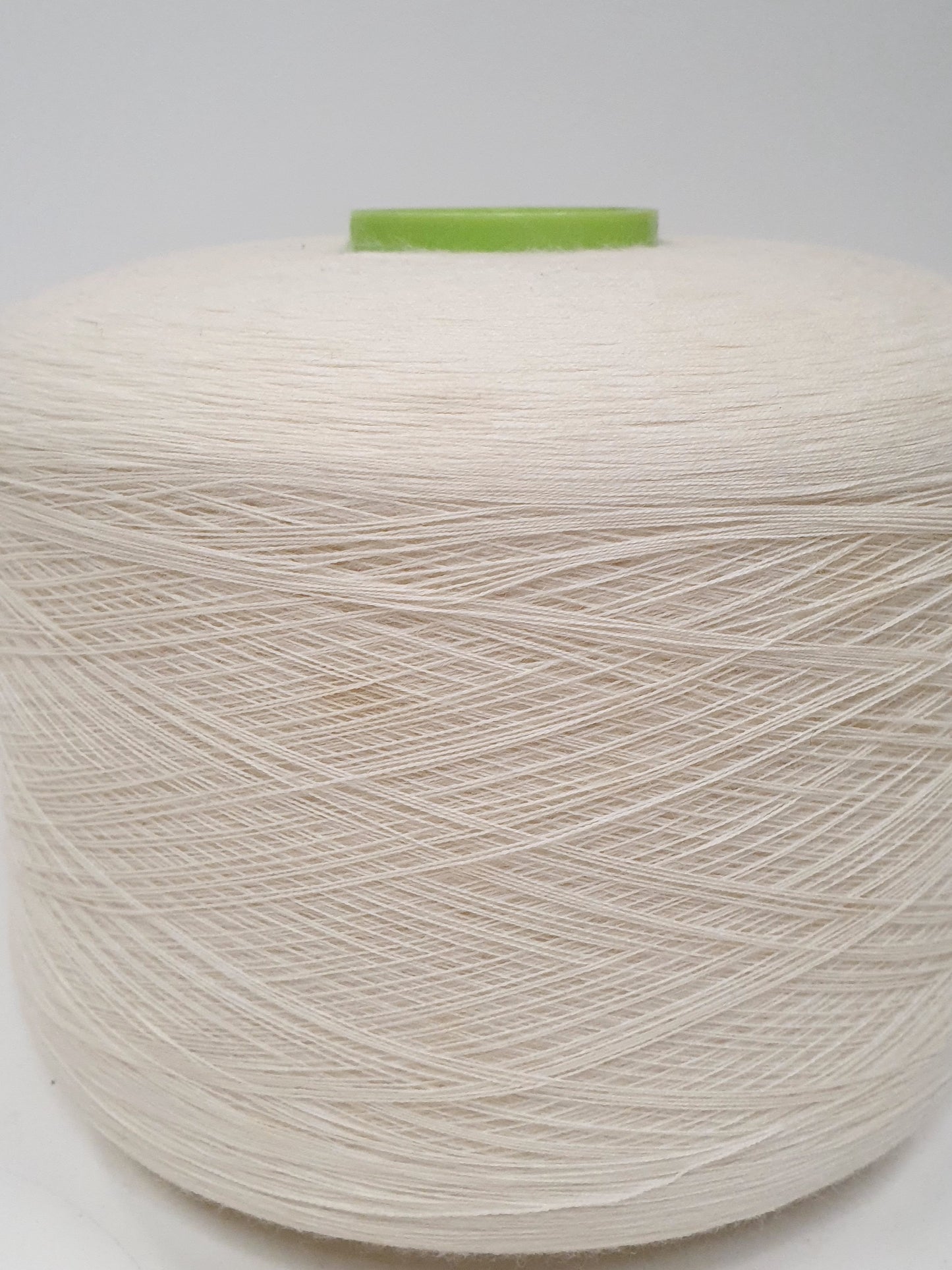 Close up of a single white yarn cone with a green cap, indicative of being used for knitting or crafting purposes. 