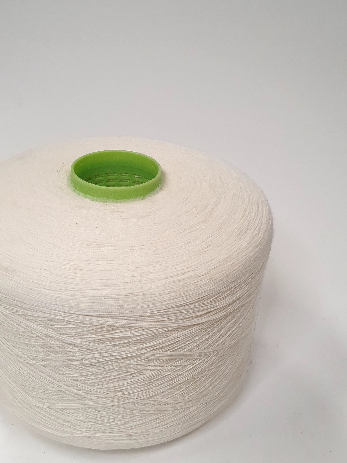 Close up of a single white yarn cone with a green cap, indicative of being used for knitting or crafting purposes. 