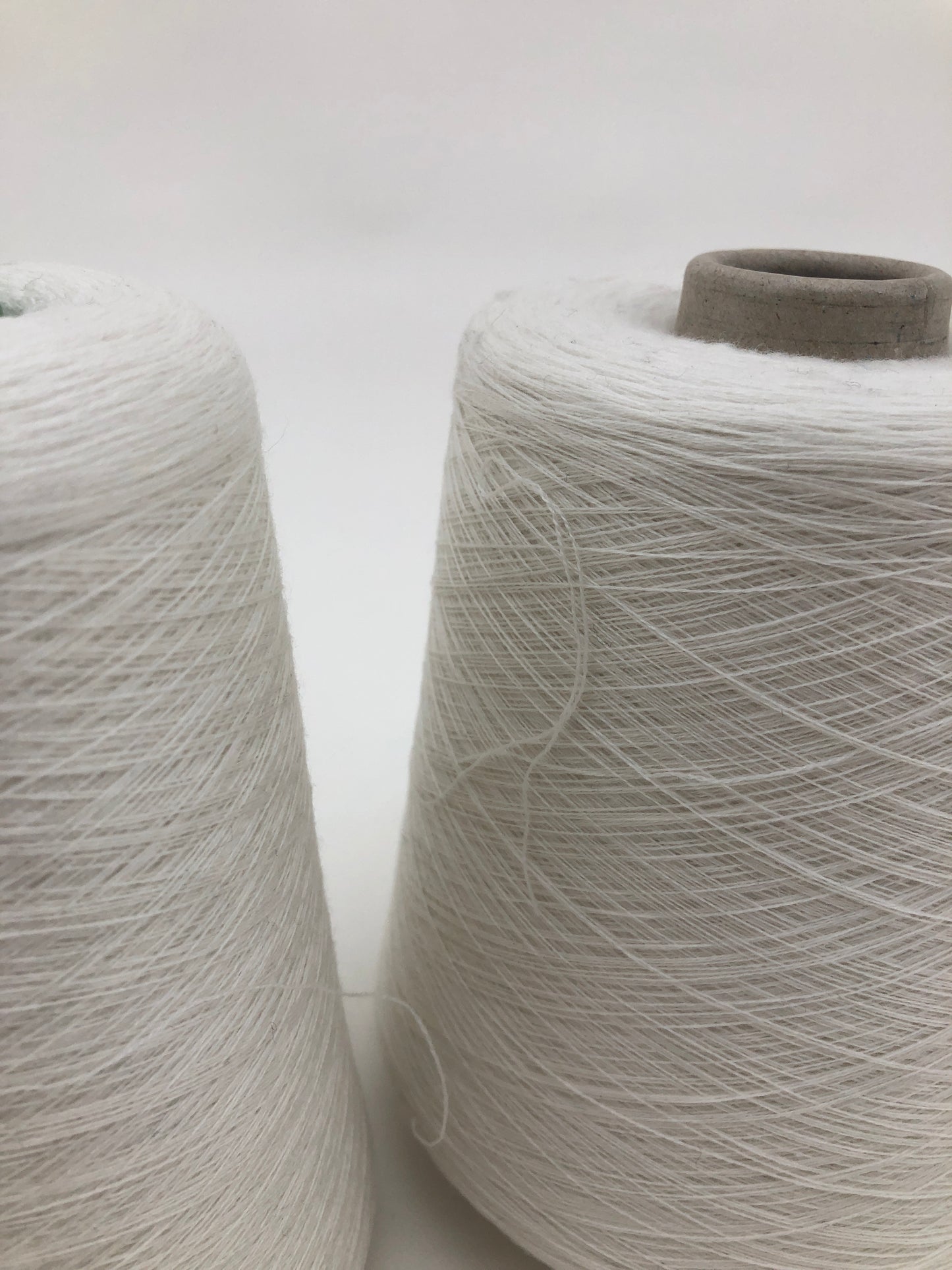 Close up of a cone of synthetic material yarn made of blended tencel, poly, etc, displayed against a white background.
