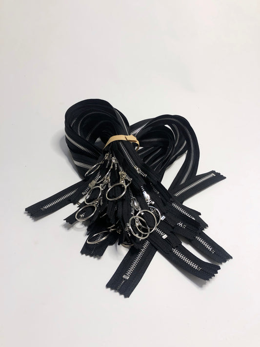 A pile of zips with ring shaped puller, black zipper tape and silver elements. 