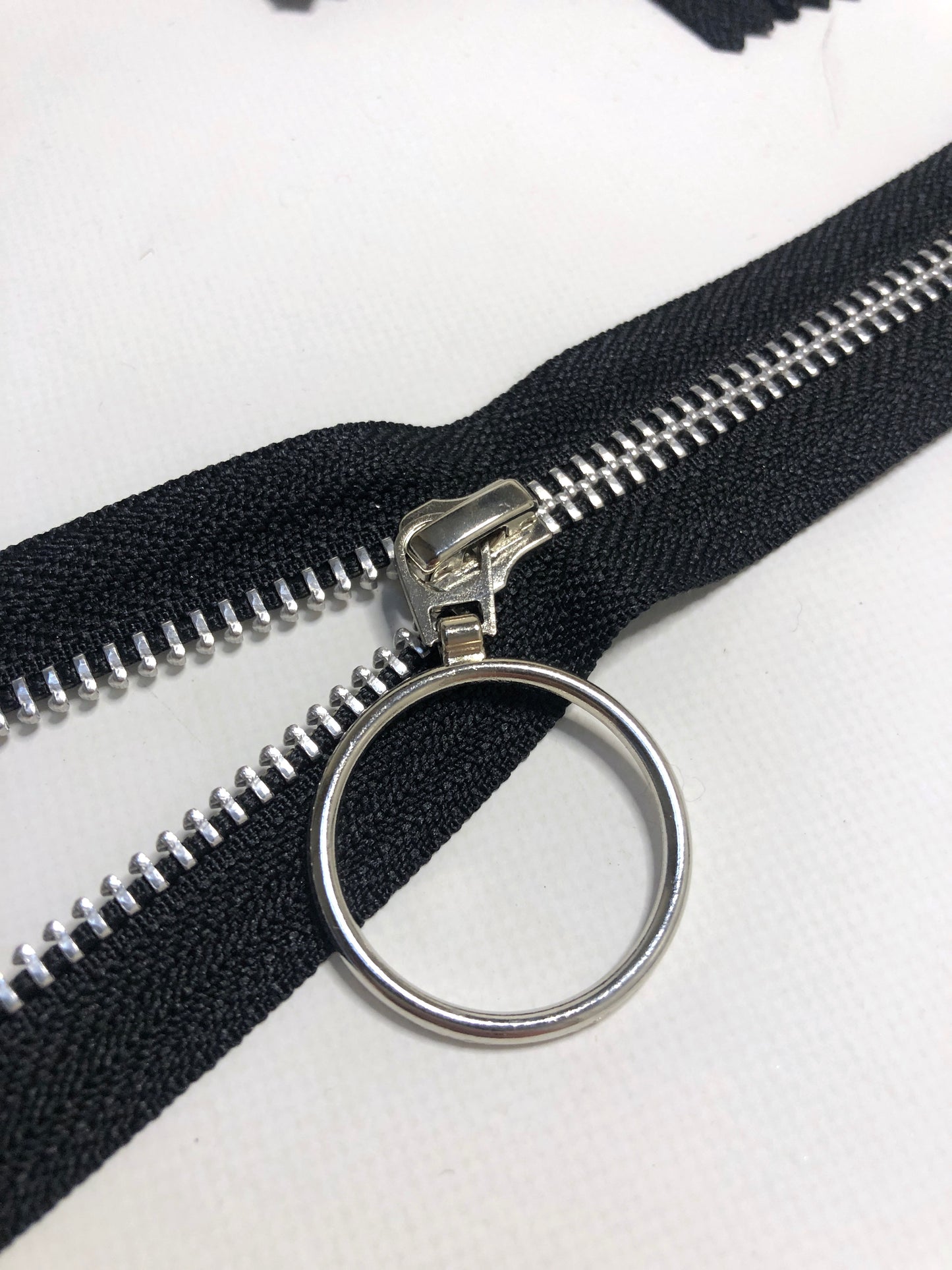 Close up of ring shaped puller, opening the black zipper tape and silver elements. 