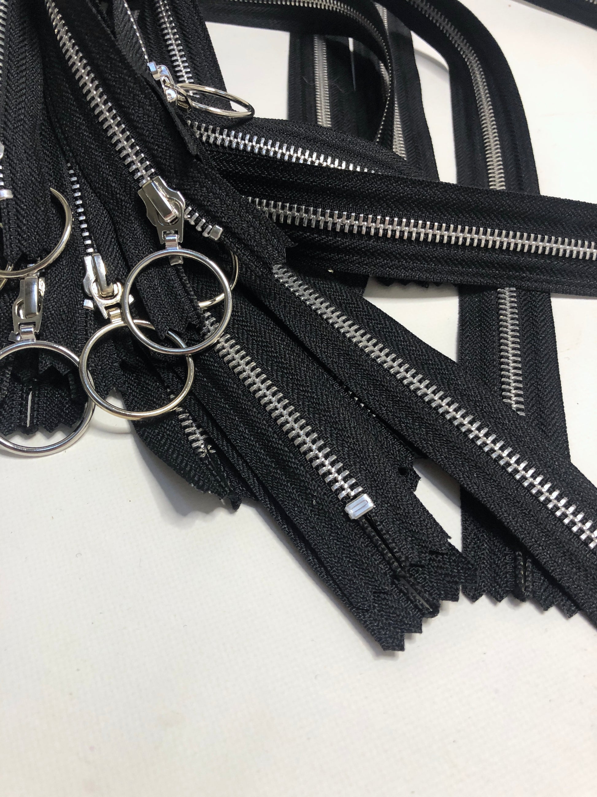 A close up pile of zips with ring shaped puller, black zipper tape and silver elements. 