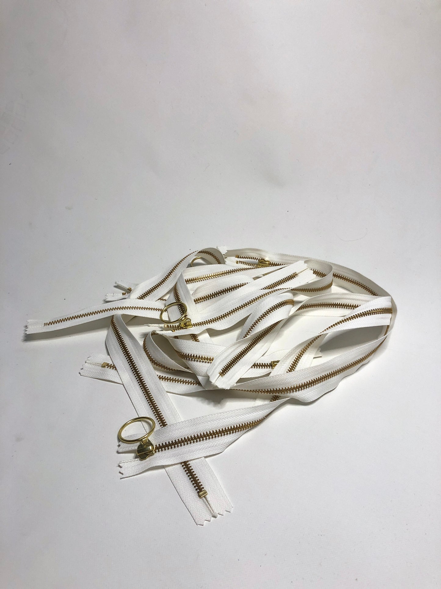 A pile of zips with ring shaped puller, white zipper tape and gold elements. 
