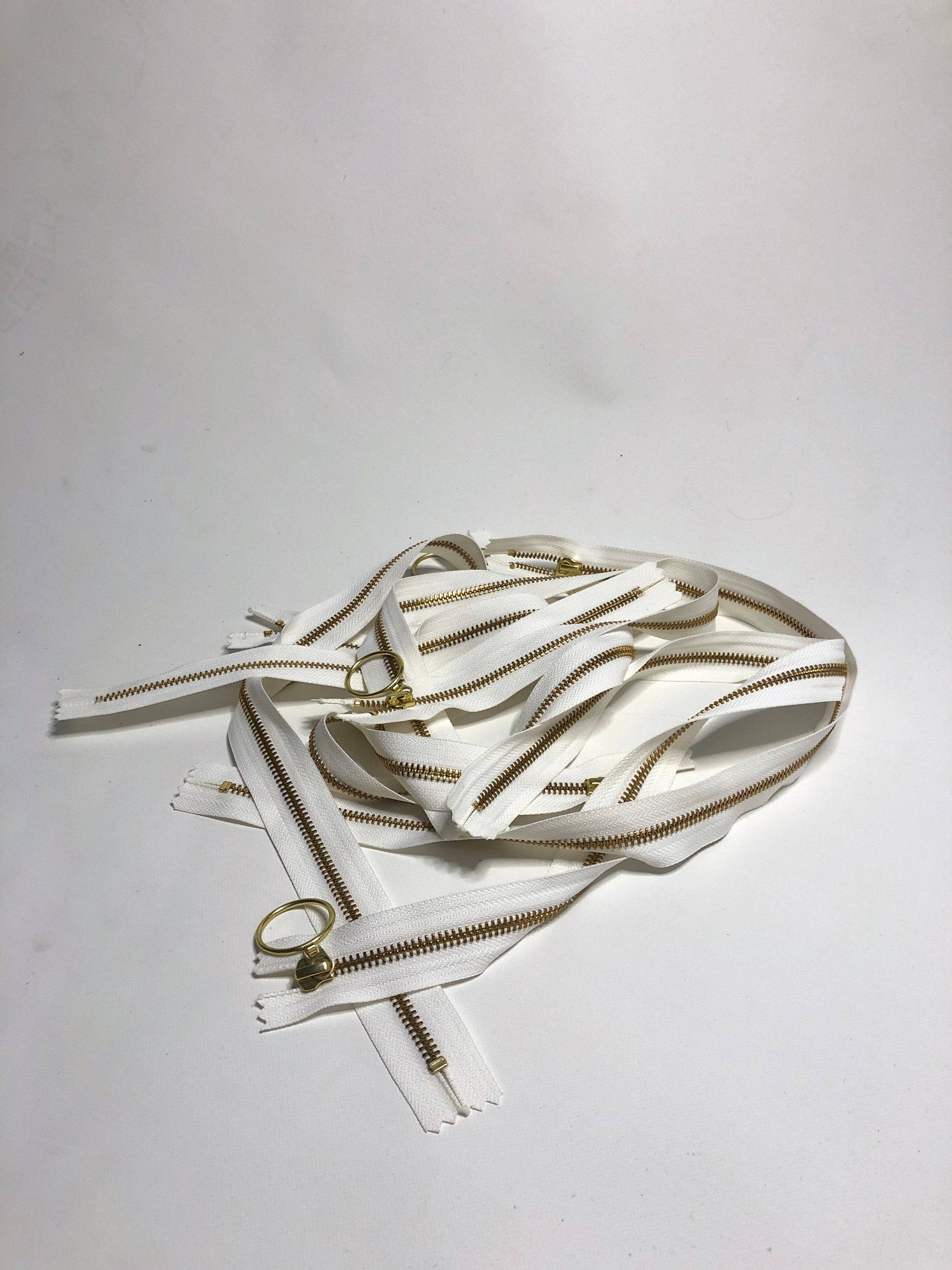 A pile of zips with ring shaped puller, white zipper tape and gold elements. 
