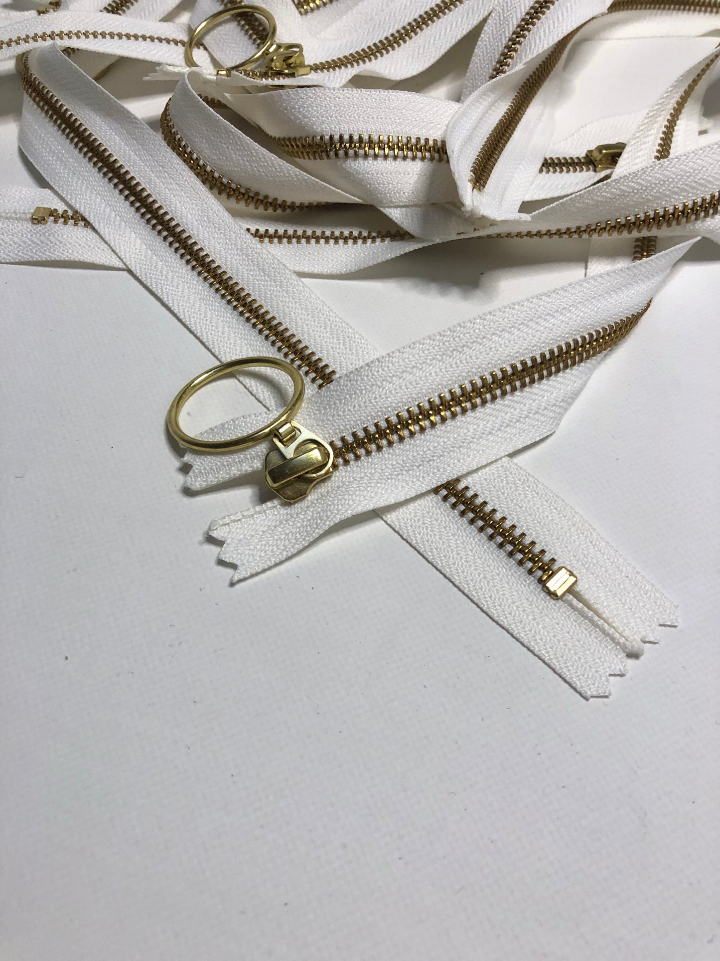 Close up of ring shaped puller, white zipper tape and gold elements. 