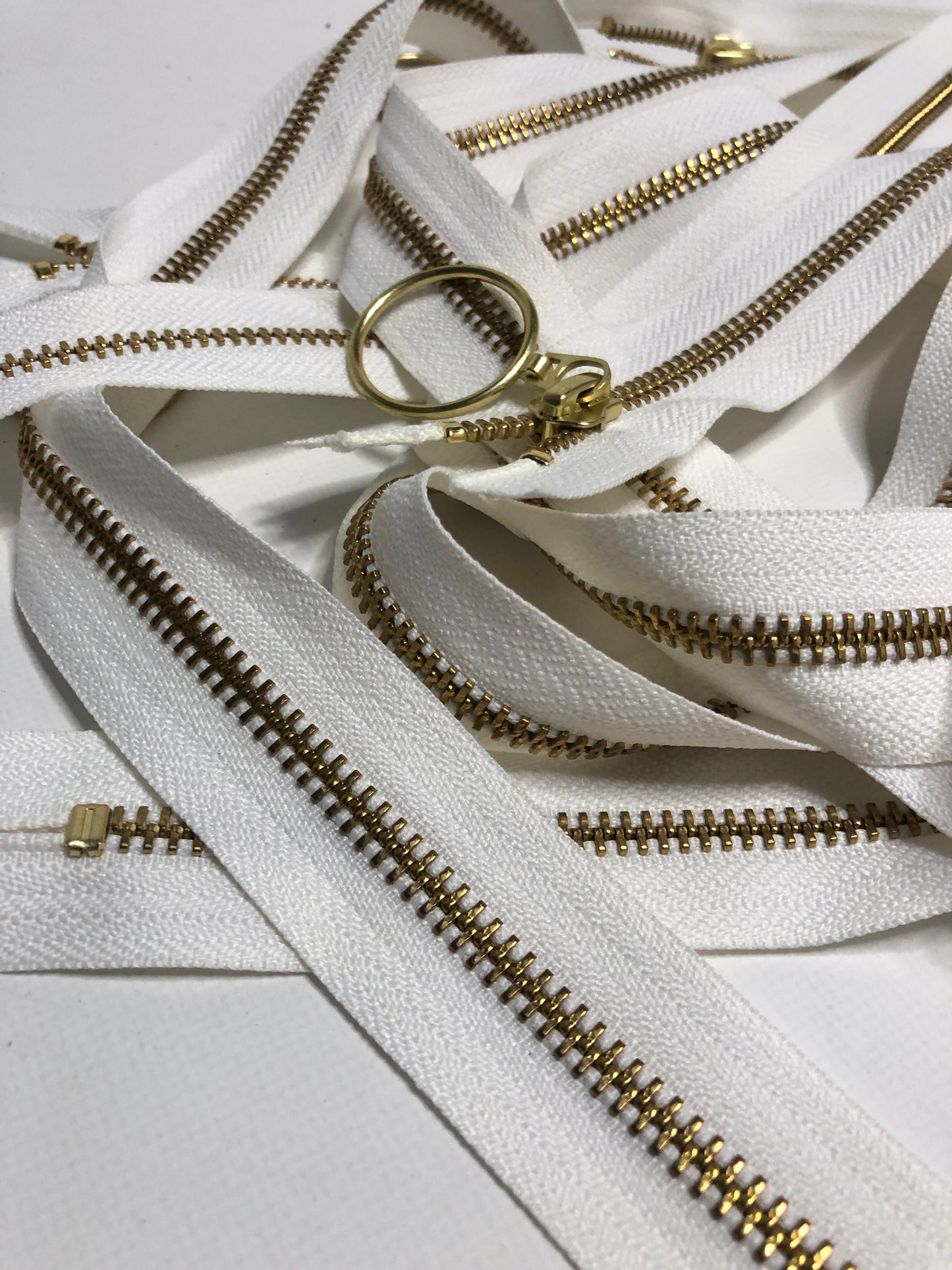 Close up of ring shaped puller, white zipper tape and gold elements. 