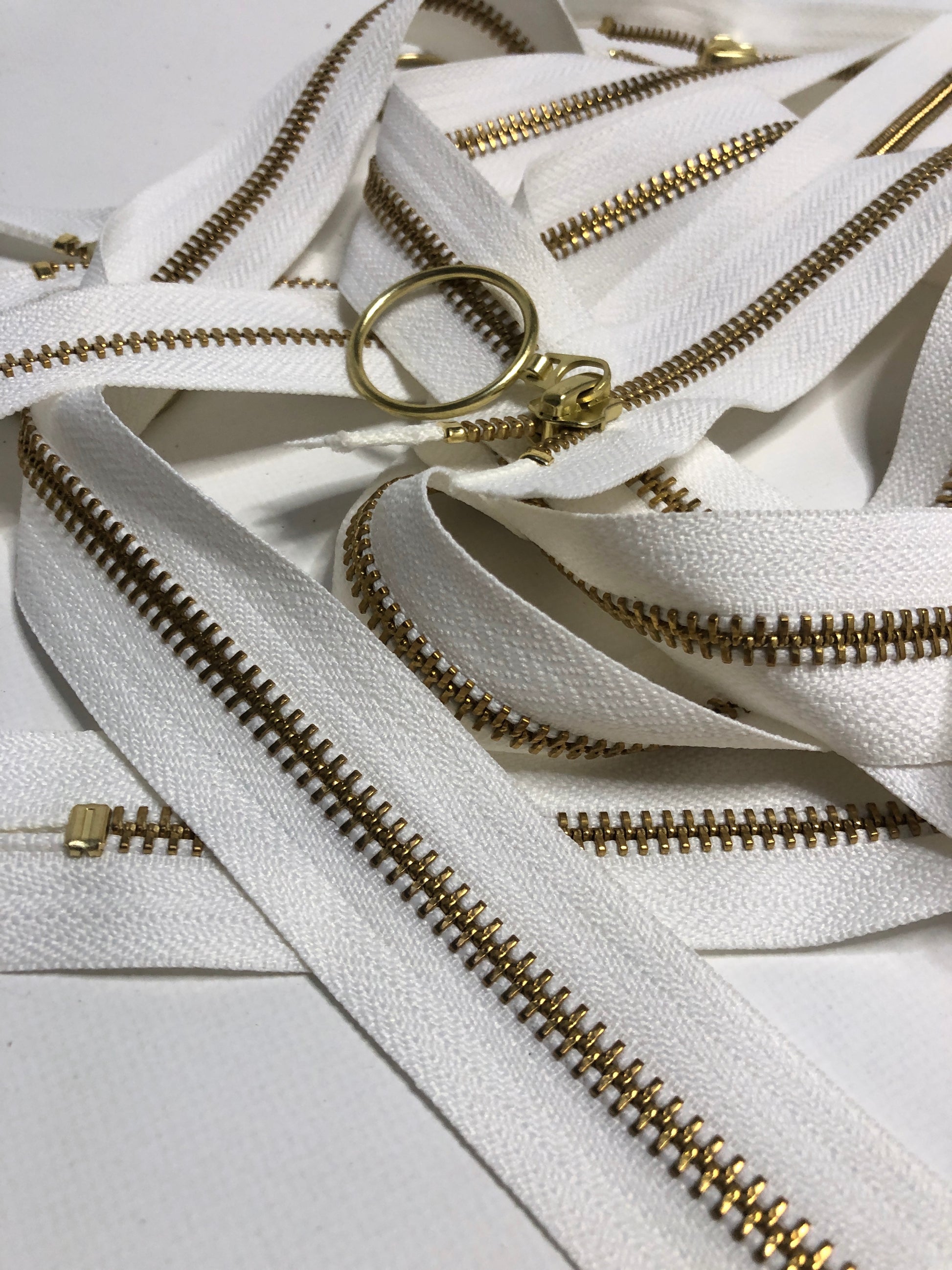 Close up of ring shaped puller, white zipper tape and gold elements. 