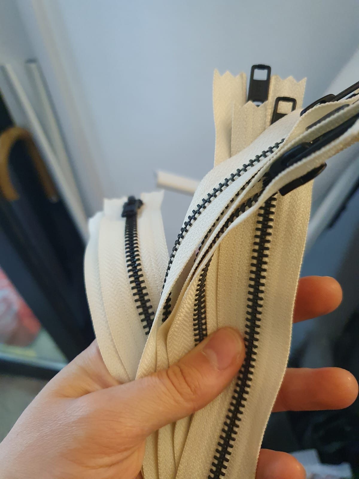 Hand holding a pile of zips with a black square shaped puller, white zipper tape and black elements. 